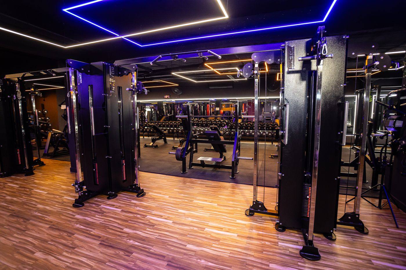 Sala de musculação com torres de cabo Tractor, piso de madeira e iluminação em neon azul
